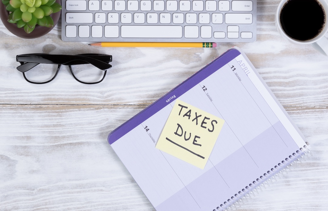 A well-organized desk with a planner opened to a page with a reminder sticky note saying "IRS LT38 Notice", accompanied by a keyboard, glasses, pencil, and a cup of coffee.