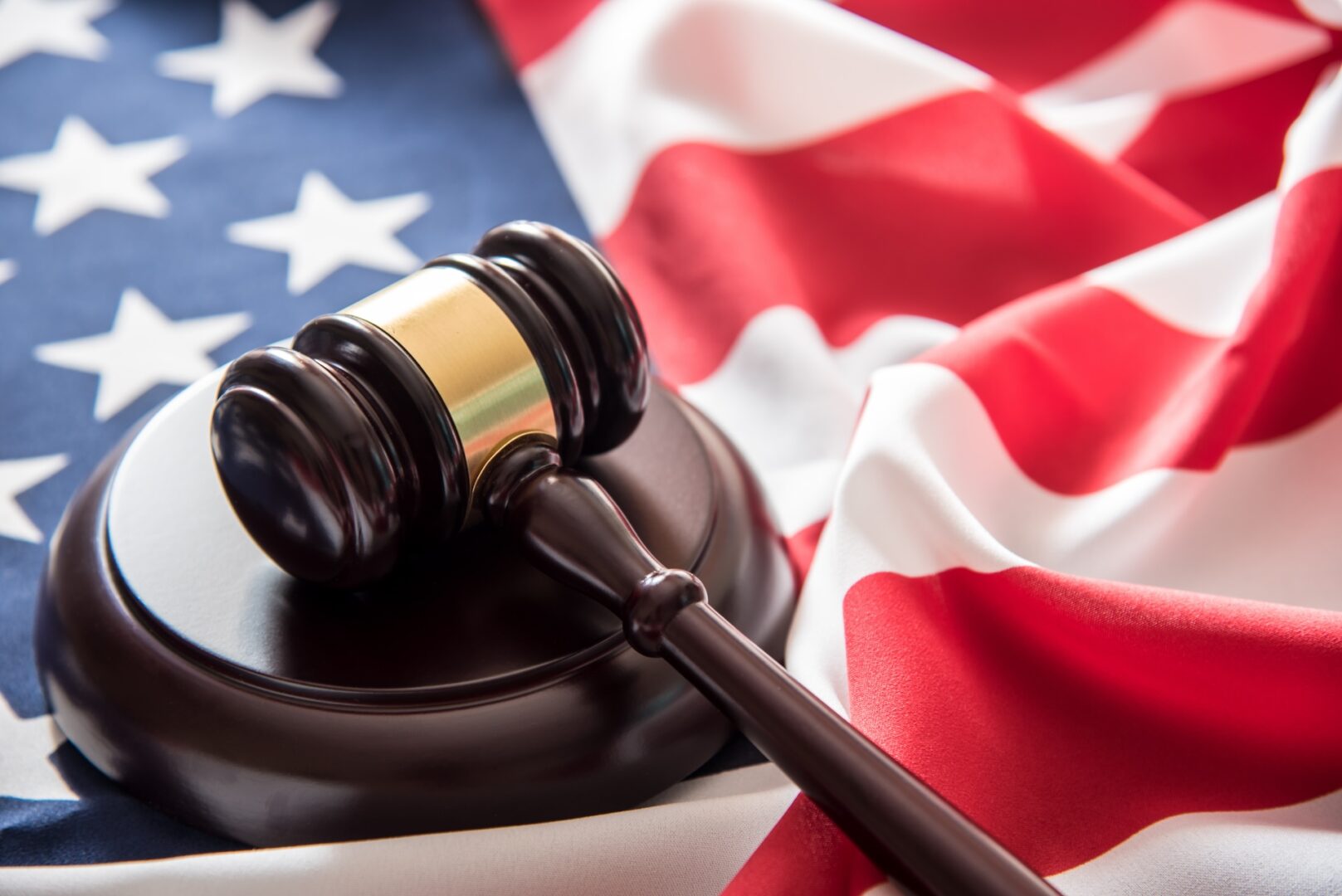 A wooden gavel rests on a sound block, placed on a partially visible American flag with stars and stripes. The image conveys themes of justice and law in the United States.