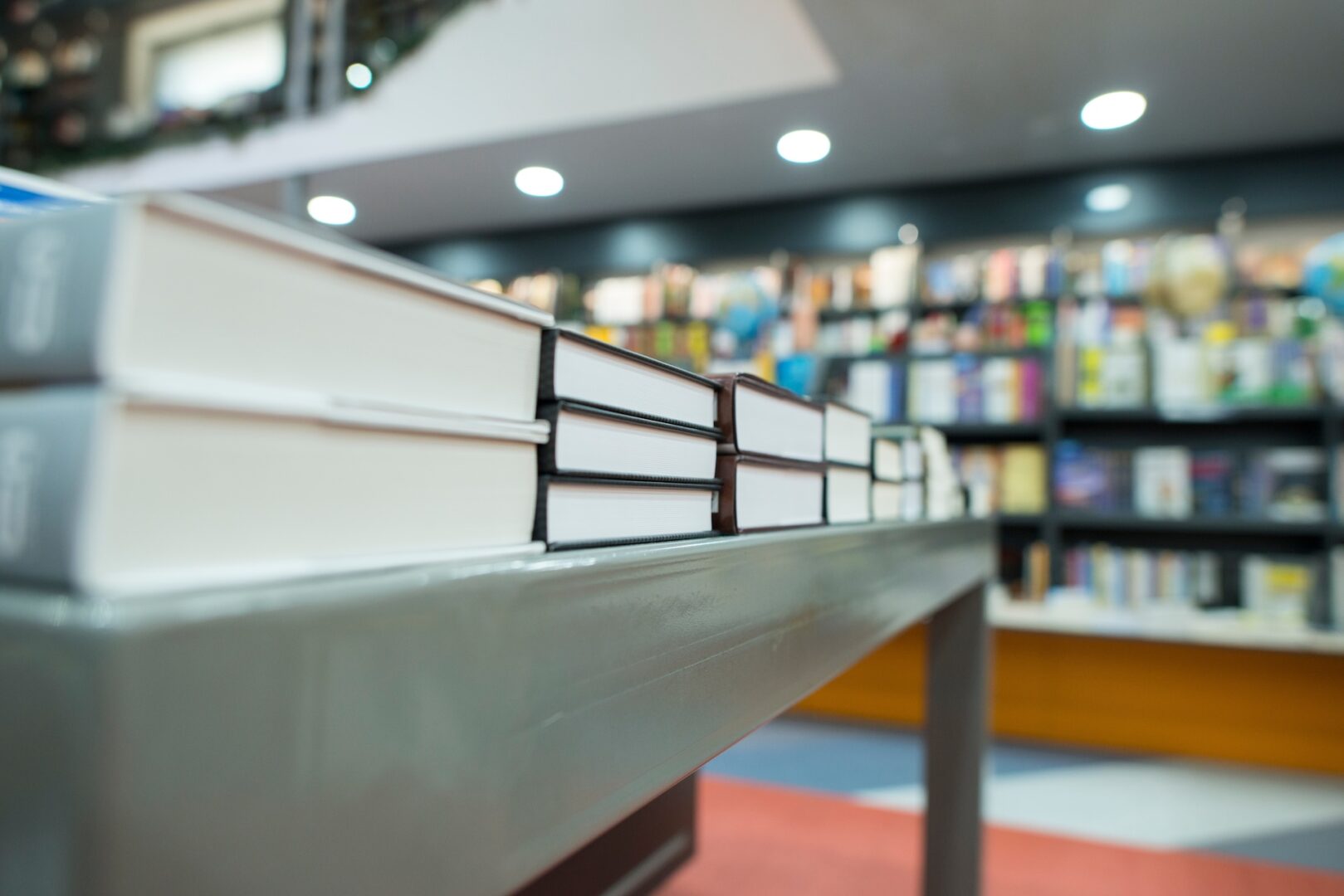 A row of books lies on a table in a bookstore, with shelves of books in the blurred background. The focus is on the spines and pages of the books, highlighting the depth of the collection.