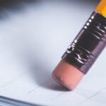 A close-up of a pencil eraser gently rubbing on white paper, with faint lines visible on the page and the yellow pencil barrel partially shown—much like making tax amendments to correct errors.