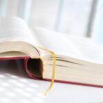 Our Comprehensive Guide to Prepare For a Tax Audit lies open—a large hardcover with a red spine and yellow ribbon bookmark—on a white surface, bathed in soft sunlight that creates a dappled pattern across the pages.