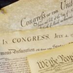 Close-up of historical U.S. documents, including the Declaration of Independence and Constitution, with an American flag and a quill pen—reminding us that IRS tax debt over $10,000? Why you might need a lawyer to protect your rights.
