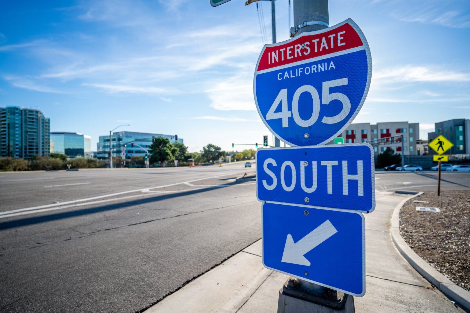 A blue and red Interstate 405 South sign for California stands at a street corner, with modern buildings and a crosswalk in the background on a clear, sunny day. A blue and red Interstate 405 South sign for California stands at a street corner, with modern buildings and a crosswalk in the background on a clear, sunny day.