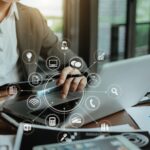 A person in business attire uses a laptop at a desk with papers, coffee, and a pen. Digital network and technology icons are overlaid, highlighting connectivity, data, and ways to maximize 2025 stock market gains with these tax tips.