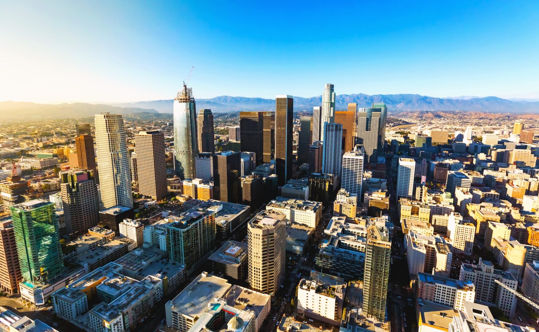 Aerial view of a city skyline with tall skyscrapers, dense urban buildings, and mountains in the background under a clear blue sky. Aerial view of a city skyline with tall skyscrapers, dense urban buildings, and mountains in the background under a clear blue sky.