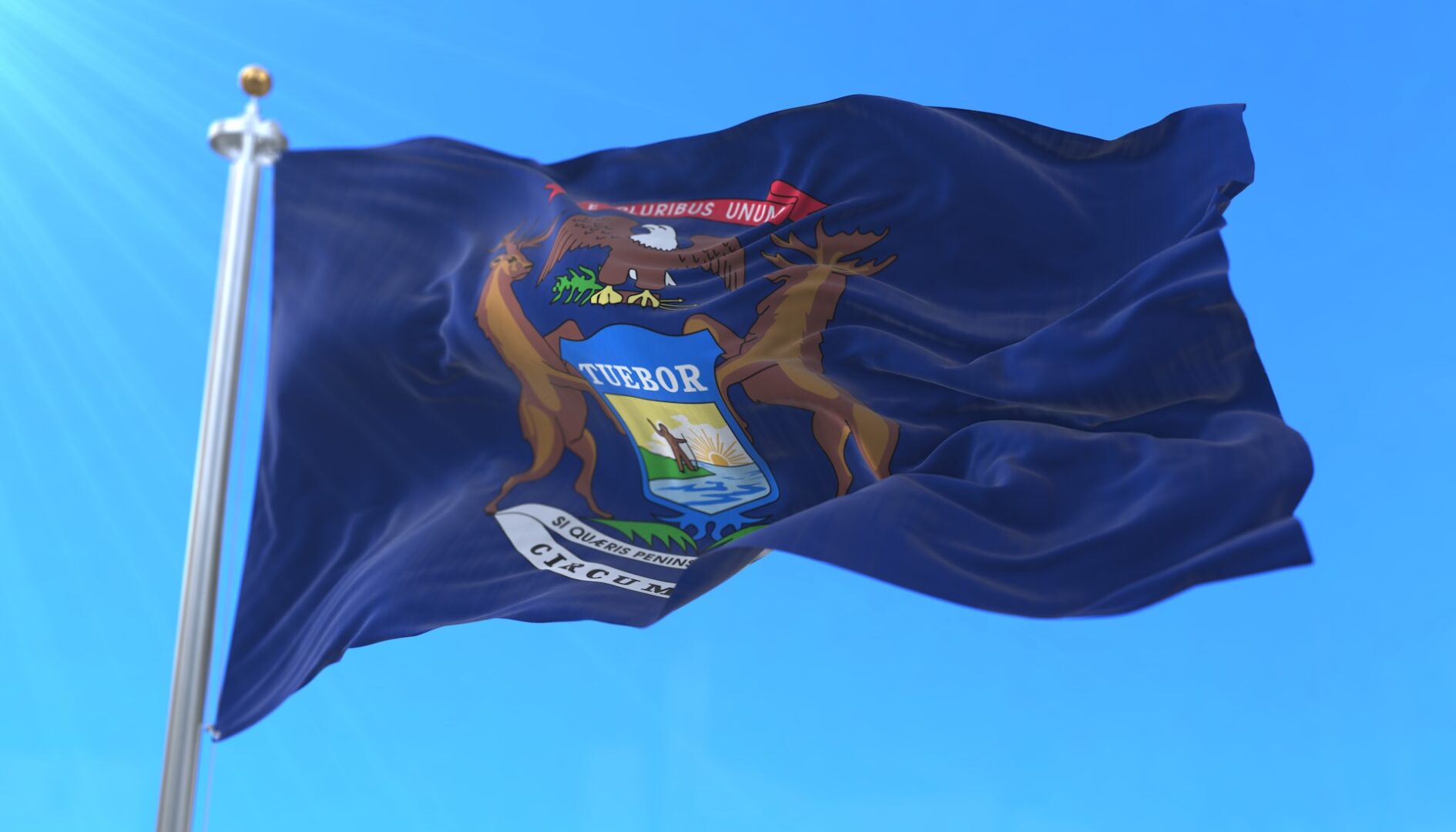 The Michigan state flag waves against a clear blue sky, displaying the state’s coat of arms with an eagle, elk, moose, and shield featuring a man, water, and a sun. The Michigan state flag waves against a clear blue sky, displaying the state’s coat of arms with an eagle, elk, moose, and shield featuring a man, water, and a sun.