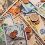 Various international paper currencies, including US dollars, euros, and others, are scattered on a surface with coins of different denominations—an ideal reminder to maximize 2025 stock market gains with these tax tips.