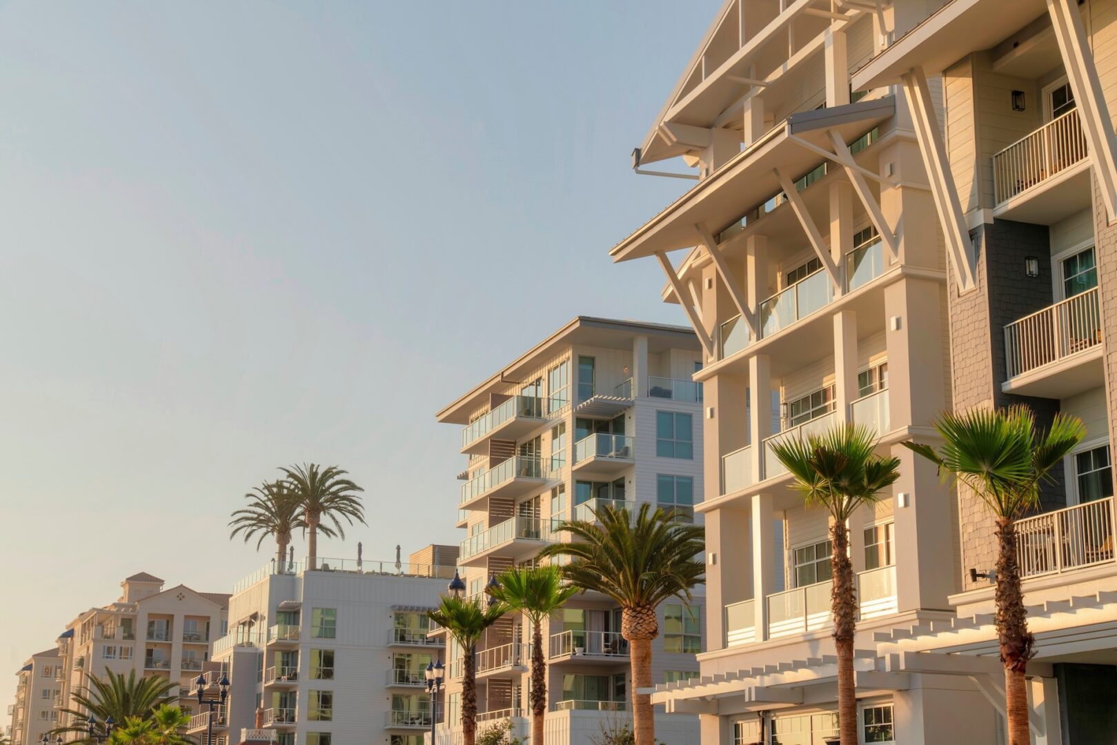 Modern apartment buildings with balconies lined with tall palm trees under a clear sky, lit by warm sunlight. Modern apartment buildings with balconies lined with tall palm trees under a clear sky, lit by warm sunlight.