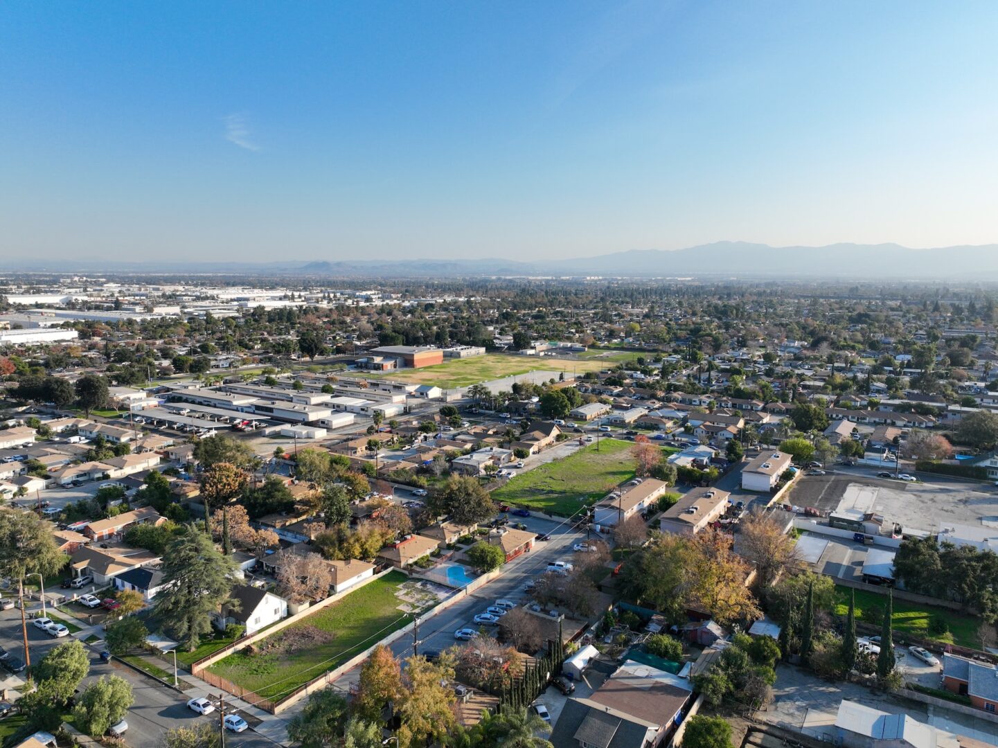 Aerial view of a suburban neighborhood with houses, streets, and green spaces, under a clear blue sky with distant mountains visible on the horizon. Aerial view of a suburban neighborhood with houses, streets, and green spaces, under a clear blue sky with distant mountains visible on the horizon.