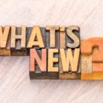 Wooden letter blocks arranged to spell out "WHAT'S NEW?" are placed on a light wooden surface, highlighting Pietro Canestrelli Featured in Hustle Weekly for Humanizing Tax Law. The text is in various shades of brown and orange.