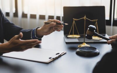 Two people in suits sit at a desk with a clipboard, golden scales of justice, and a judge's gavel, discussing how Business Formation & Tax Planning Lawyers set startups up for success in a well-lit office.