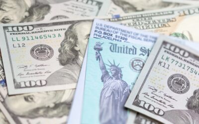 A close-up of U.S. $100 bills and a U.S. Treasury check, featuring the Statue of Liberty, arranged in a scattered manner—perfect for illustrating topics like Fight Back Against the IRS: Lawyer & Ex-Agent Guide to Appeals.