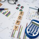 A desk with charts, graphs, a blue calculator, pen, glasses, small clock, and wooden letter tiles spelling "EOFY," representing end-of-financial-year business tasks—plus tips to Get $1,000 More on Your 2026 Tax Refund & Here's How.