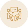 An icon showing two people sitting at a table facing each other with a speech bubble above them, suggesting a conversation or meeting, on a beige circular background.