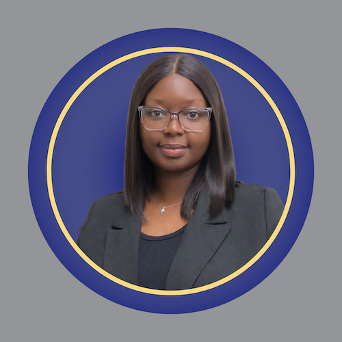 A woman with straight, shoulder-length hair and glasses, wearing a dark blazer over a black top, poses against a blue background with a gold-edged circular border. A woman with straight, shoulder-length hair and glasses, wearing a dark blazer over a black top, poses against a blue background with a gold-edged circular border.
