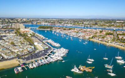 Aerial view of a marina with numerous boats docked, surrounded by waterfront homes and buildings under a clear blue sky. The winding waterway showcases the vibrant city where finding a trusted Tax Attorney in Newport Beach is easy.
