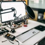 A close-up of a podcast recording setup on a desk, featuring a microphone with pop filter, an audio recorder, a computer keyboard, and a monitor—perfect for discussing content creator tax problems.