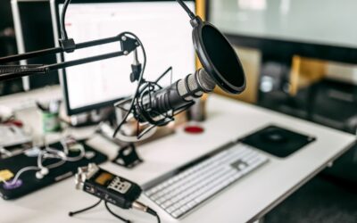 A close-up of a podcast recording setup on a desk, featuring a microphone with pop filter, an audio recorder, a computer keyboard, and a monitor—perfect for discussing content creator tax problems.