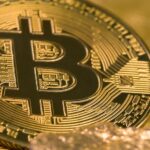 Close-up of shiny gold-colored Bitcoin tokens surrounded by small gold nuggets, placed on a textured golden surface.