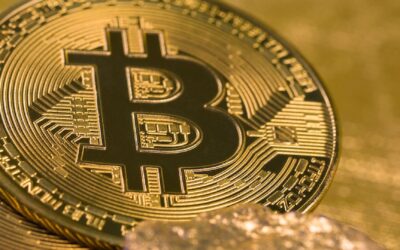 Close-up of shiny gold-colored Bitcoin tokens surrounded by small gold nuggets, placed on a textured golden surface.