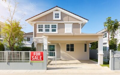 Modern two-story house with beige siding and white trim, a covered carport, and a gated driveway. A red “For Sale” sign is displayed on the front fence. Trees and neighboring houses are visible.