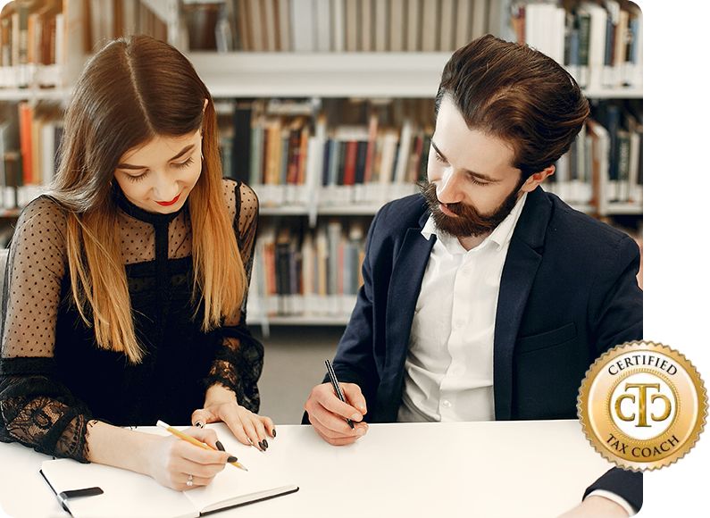 A woman and a man sit at a table in a library, both writing in notebooks. The woman has long brown hair and wears a black blouse, while the man has a beard and wears a suit. A "Certified Tax Coach" badge is in the corner.