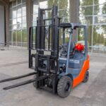 A red and black forklift is parked outside a modern building with large glass windows. The forklift's forks are raised slightly off the ground, and trees are reflected in the windows behind it.