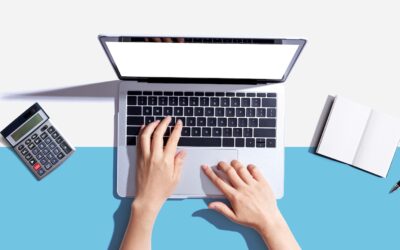Top view of hands typing on a laptop keyboard, with a calculator on the left, an open notebook, and a pen on the right, all on a white and blue background.